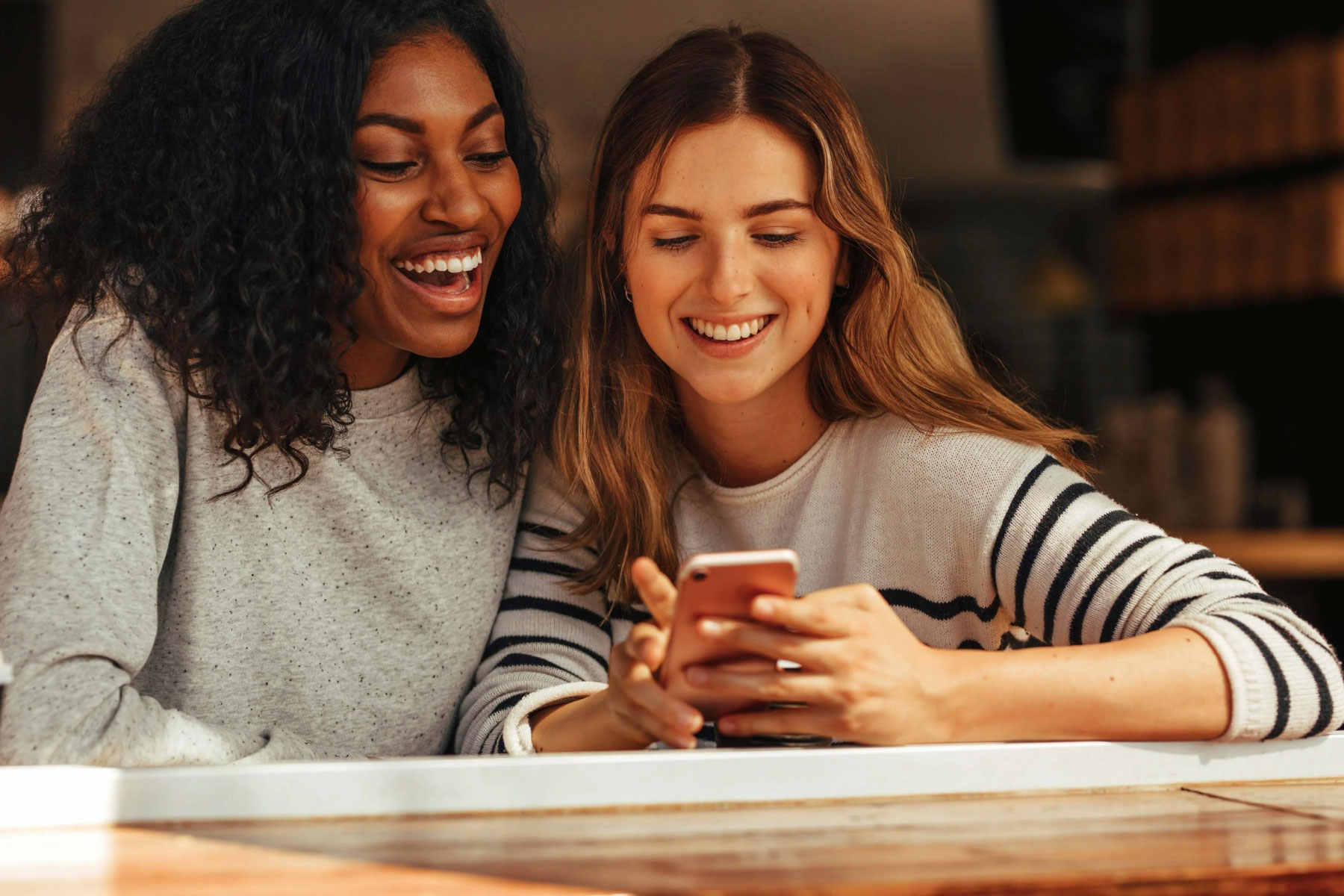 Two female college students looking at one smartphone together while smiling