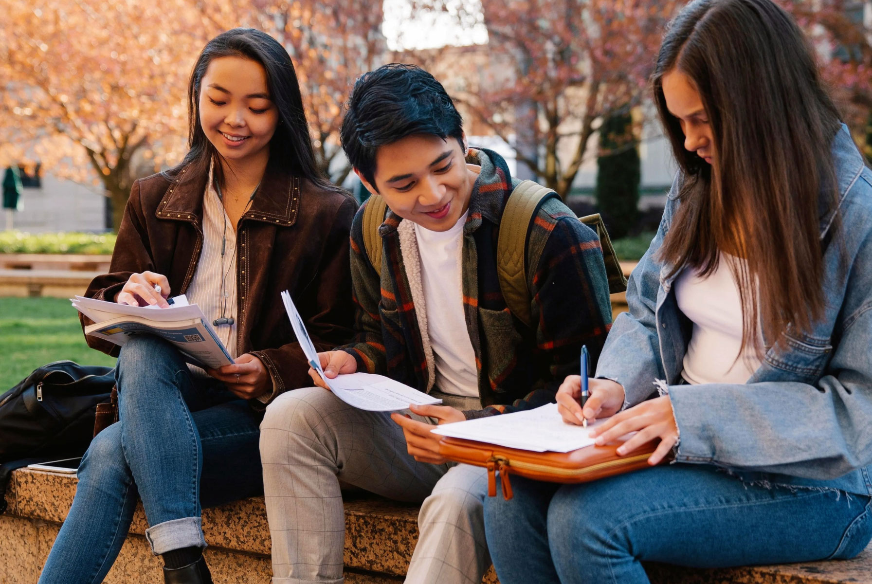 Group of students smiling while sitting on bench outside and studying together